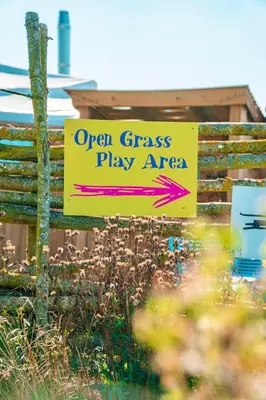 an open grass play area sign in front of a building at Hatters Meadows Glamping in Ely