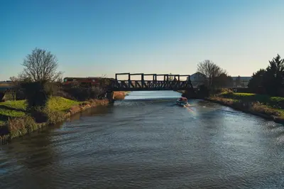 a boat traveling down a river under a bridge at Hatters Meadows Glamping in Ely