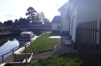 a boat parked next to a building next to a canal at Cottage - Sleeps 3 Parking & Fishing in Hilgay