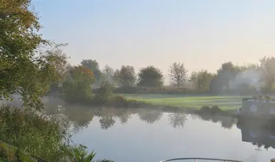 a misty river with a golf course in the background at Cottage - Sleeps 3 Parking & Fishing in Hilgay