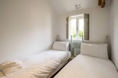two beds in a white room with a window at East Green Farm Cottages - The Old Stables in Saxmundham