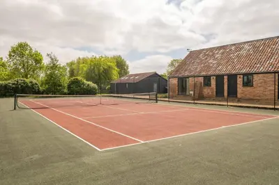 a tennis court in front of a house at East Green Farm Cottages - The Granary in Saxmundham