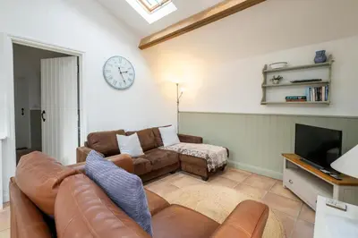 a living room with a couch and a clock on the wall at East Green Farm Cottages - Gardeners Cottage in Saxmundham