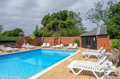 a swimming pool with lounge chairs and a building at East Green Farm Cottages - Gardeners Cottage in Saxmundham