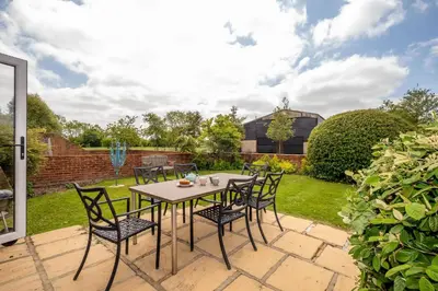 a patio with a table and chairs in a garden at East Green Farm Cottages - The Hayloft in Saxmundham