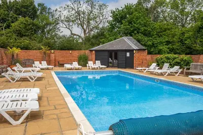 a swimming pool with white lounge chairs and a house at East Green Farm Cottages - The Hayloft in Saxmundham