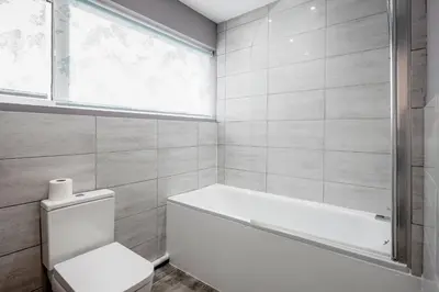 a bathroom with a toilet and a tub and a window at Remaj Serviced Accommodation, sleeps 7 & free parking in Laindon