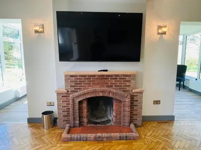 a living room with a brick fireplace with a flat screen tv at Warren Lodge in Little Baddow