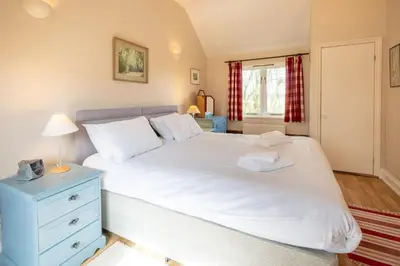 a bedroom with a white bed with a blue dresser and a window at The Stables, Theberton in Theberton