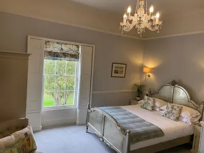 a bedroom with a bed with a chandelier and a window at Reymerston Hall in Norwich