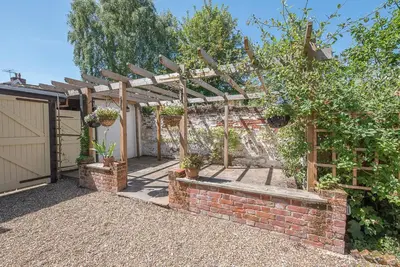 a garden with a brick wall and a wooden pergola at Abigail's Cottage, Wickham Market in Woodbridge