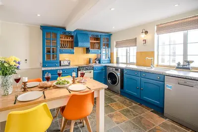a blue kitchen with a wooden table and yellow chairs at Abigail's Cottage, Wickham Market in Woodbridge