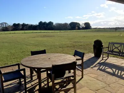 a wooden table and chairs with a field in the background at White Cottage Apartment in Snape