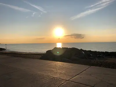 a sunset on the beach with the sun setting over the ocean at Tref y Clawdd in Felixstowe