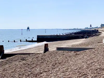 a beach with a pier and people in the water at Mayflower Cottage in Harwich