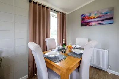 a dining room with a wooden table and white chairs at Sea Cloud in Aldeburgh