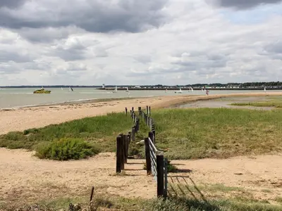 a wooden fence on a beach with people in the water at Curlew in Brightlingsea