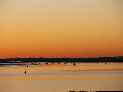 an orange sunset over a beach with boats in the water at Curlew in Brightlingsea