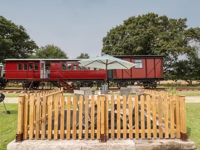 a wooden fence with an umbrella in front of a train at The Carriage at High Barn Heritage in Halstead
