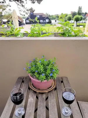 a potted plant on a wooden table with two wine glasses at Regatta - A lakeview apartment in Thorpeness - Aldeburgh Coastal Cottages in Thorpeness