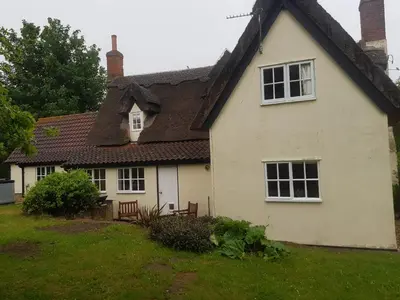 a white house with a black roof at Burnt House Cottage in Barking