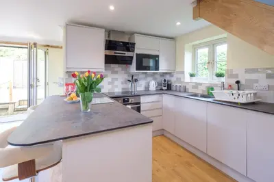 a kitchen with white cabinets and a vase of flowers on a counter at Foxes Lodge in Aldringham