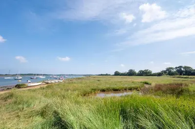 a field of grass with boats in the water at 1 Bed in Waldringfield oc-thstu in Waldringfield