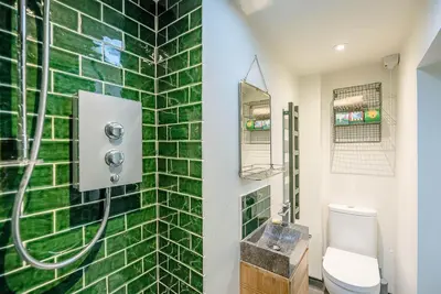 a bathroom with a toilet and a green tiled wall at The Wash House, Middleton in Saxmundham