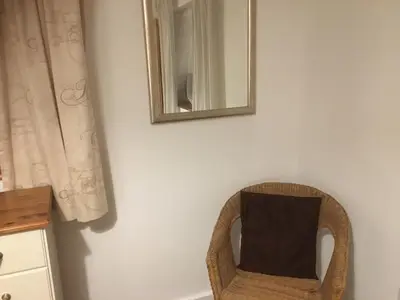 a mirror on a wall next to a wicker chair at Stone Cottage in Nazeing