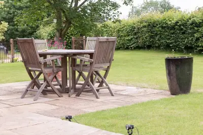two chairs and a wooden table in a garden at Immaculate barn annexe close to Stansted Airport in Great Dunmow