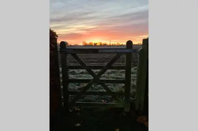 a gate to a field with a sunset in the background at Immaculate barn annexe close to Stansted Airport in Great Dunmow