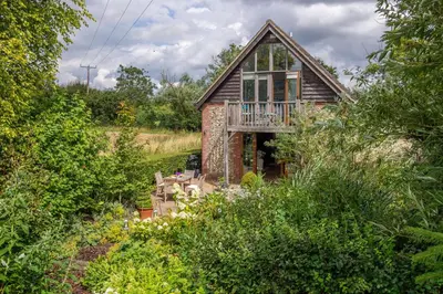 a brick house with a balcony in the middle of trees at The Granary, Dunstall Green in Denham
