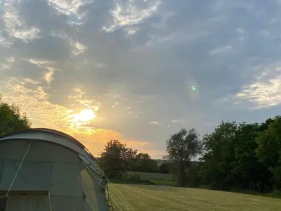 a tent in a field with the sunset in the background at Rockinghams Farm in Layer Marney