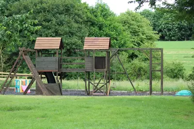 a playground in a park with two wooden swings at Little Oaks in Stowmarket