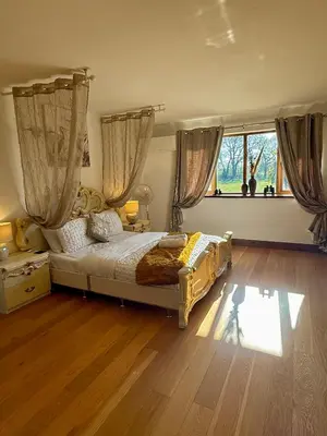 a bedroom with a bed with curtains and a wooden floor at Barnfields Retreat in Little Clacton