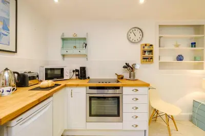 a kitchen with white cabinets and a clock on the wall at Theberton Cottage in Theberton