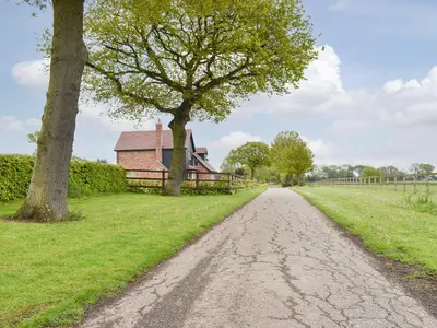 a dirt road in front of a barn and a tree at Leveret Lodge in Burgh