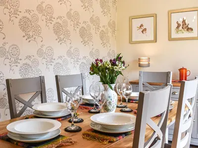 a dining room table with plates and glasses and flowers at Beck Cottage in Mildenhall