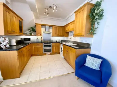 a kitchen with wooden cabinets and a blue chair at Coastal Mews House close to Beach in Felixstowe
