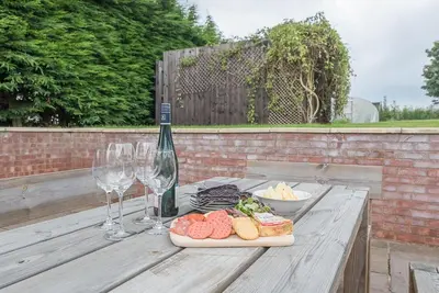 a wooden table with wine glasses and food on it at Grove Farm Bungalow with swimming pool, Dallinghoo in Woodbridge