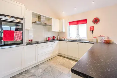 a kitchen with white cabinets and a black counter top at Grove Farm Bungalow with swimming pool, Dallinghoo in Woodbridge