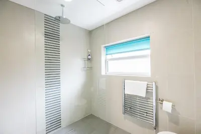 a white bathroom with a shower and a window at Grove Farm Bungalow with swimming pool, Dallinghoo in Woodbridge