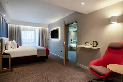 a hotel room with a bed and a red chair at Holiday Inn Express Cambridge West - Cambourne by IHG in Cambridge