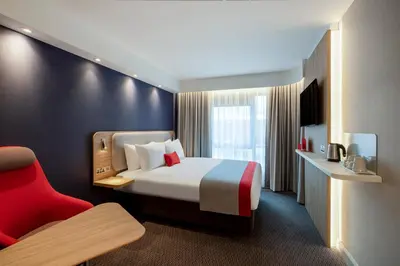 a hotel room with a bed and a red chair at Holiday Inn Express Cambridge West - Cambourne by IHG in Cambridge