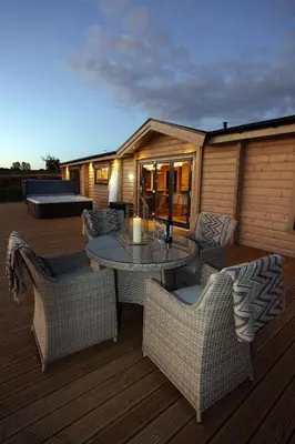 a patio with a table and chairs on a deck at Cambridgeshire Lakes - luxury lodges in a stunning lake location in Gamlingay