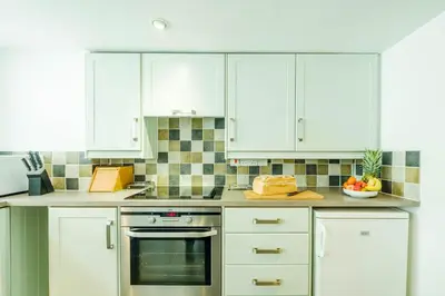 a kitchen with white cabinets and an oven at Poppy Cottage, Aldeburgh - Prime location, close to the beach and High Street - Aldeburgh Coastal Cottages in Aldeburgh