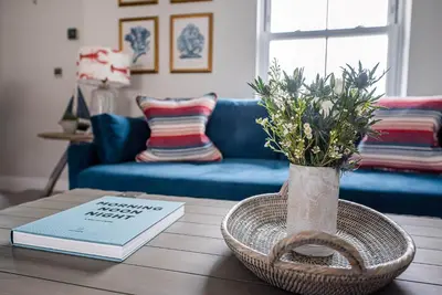 a table with a vase of flowers and a book at Pebble View, Aldeburgh in Aldeburgh