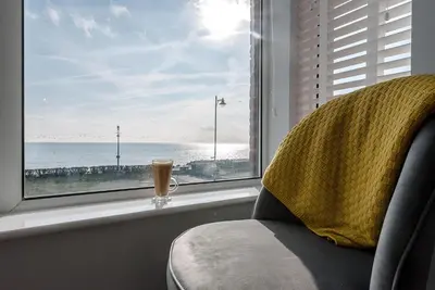 a drink sitting on a window sill with a view of the ocean at 4 Buregate House, Felixstowe in Felixstowe