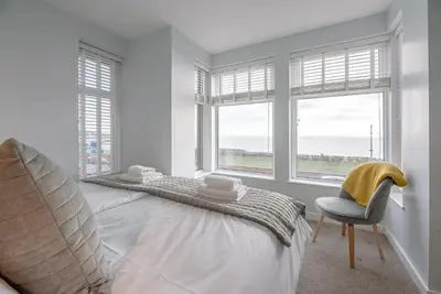 a bedroom with a bed and a chair and windows at 4 Buregate House, Felixstowe in Felixstowe