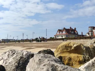 a group of rocks on a beach with a house at 4 Buregate House, Felixstowe in Felixstowe